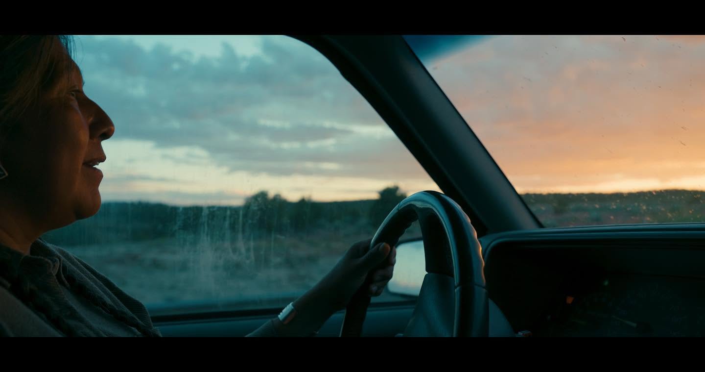 A woman driving through the desert at dusk, seen from inside the car