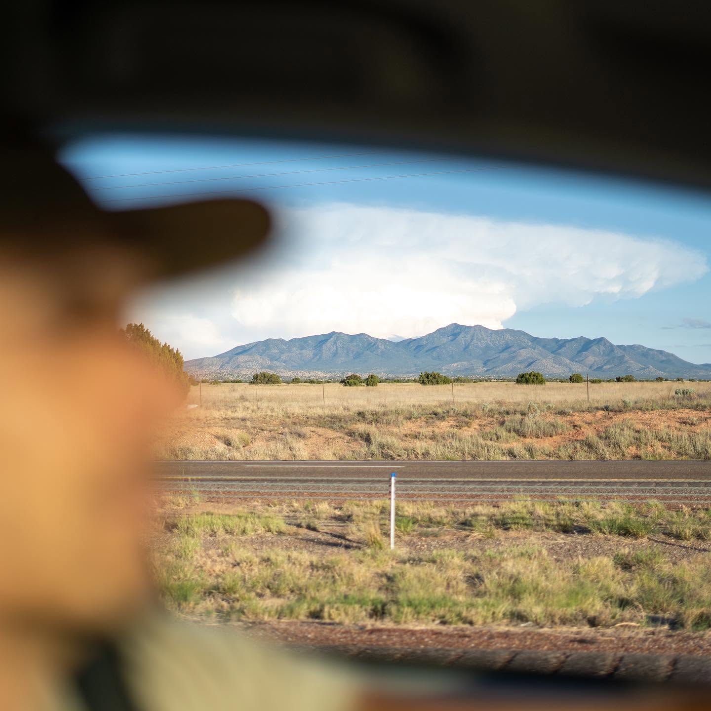 A mountain range under a wide desert sky, seen from a car window