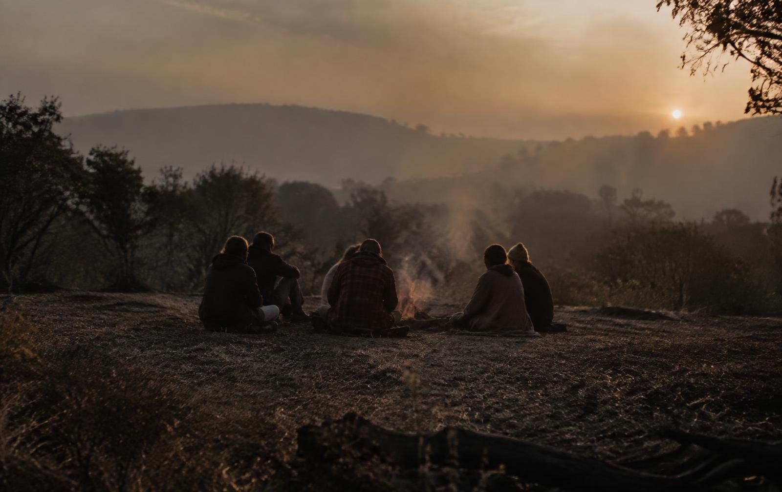 A small circle of people seated in a clearing at dusk